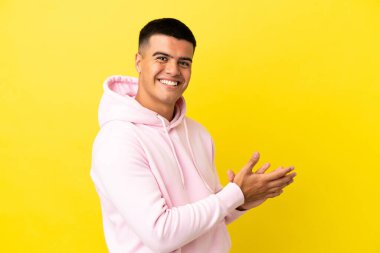 Izole sarı arka plan üzerinde genç yakışıklı adam alkışlayan