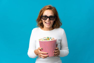 Genç Gürcü kadın mavi arka planda gözlüklü ve elinde koca bir kova patlamış mısır tutuyor.