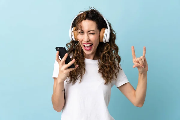 Jovem Caucasiana Isolada Fundo Azul Ouvindo Música Com Gesto Rock — Fotografia de Stock