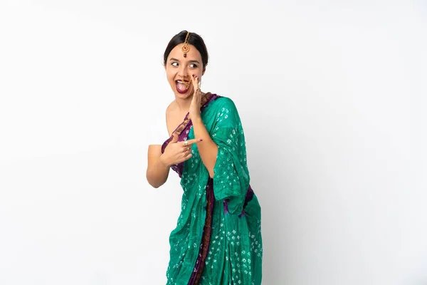 製品を提示し 何かをささやくために側面を指す白い背景に隔離された若いインドの女性 — ストック写真