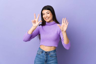 Genç esmer kadın izole edilmiş mor arka planda sekiz parmaklı sayıyor.