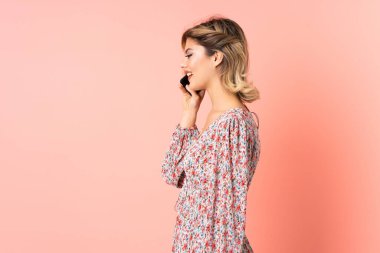 Pembe arka planda izole edilmiş genç bir Rus kadın cep telefonuyla biriyle sohbet ediyor.