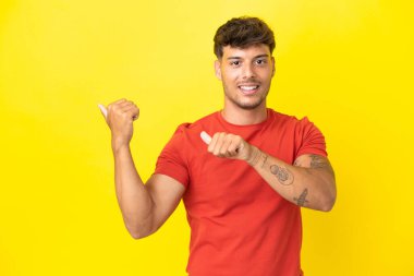 Sarı arka planda izole edilmiş beyaz, yakışıklı genç bir adam bir ürün sunmak için kenarı işaret ediyor.