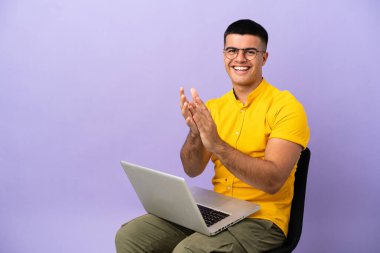 Genç adam bir konferansta sunumdan sonra dizüstü bilgisayarla oturmuş alkışlıyor.