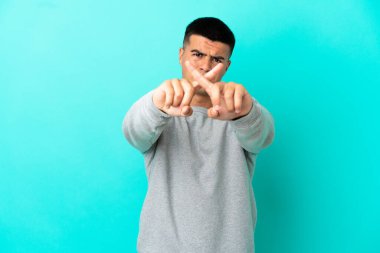 Soyutlanmış mavi arka planda genç yakışıklı bir adam bir hareketi durdurmak için eliyle jest yapıyor.