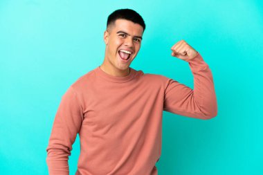 Soyutlanmış mavi arka planda genç yakışıklı adam güçlü bir jest yapıyor.