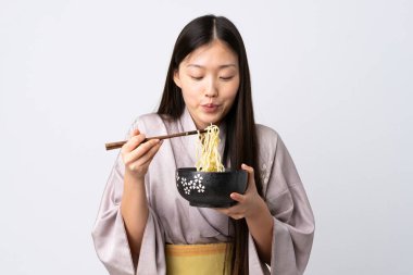 Kimono giyen genç Çinli bir kız izole edilmiş beyaz arka planda elinde çubuklu bir kase erişteyle sıcak oldukları için erişteyi üflüyor.