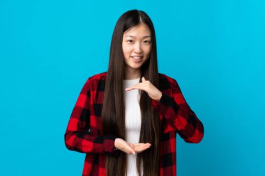 Genç Çinli bir kız, izole edilmiş mavi arka planda bir ilan vermek için avucunun içinde hayali bir mekan tutuyor.