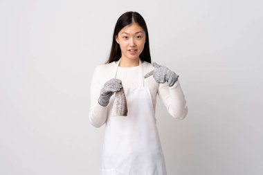 Çinli balıkçı önlük takıyor ve yüzünde sürpriz bir ifade olan beyaz arka planda çiğ balık tutuyor.