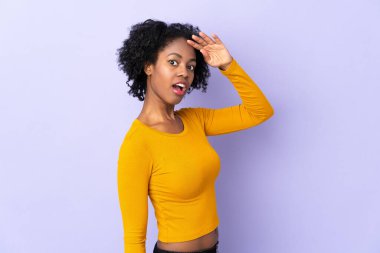 Genç Afro-Amerikalı kadın, mor arka planda yalıtılmış, sürpriz bir ifadeyle yan tarafa bakarken