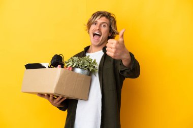 Sarışın adam sarı arka planda izole edilmiş şeylerle dolu bir kutuyu kaldırırken hareket ediyor çünkü iyi bir şey oldu.