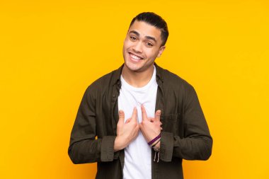 Asyalı yakışıklı adam sarı arka planda izole edilmiş, şaşırmış ve işaret ediyor.