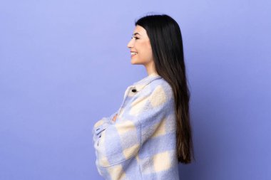 Genç esmer kadın, izole edilmiş mor arka planda yan pozisyonda.