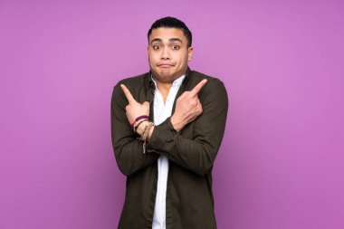 Asyalı yakışıklı adam mavi arka planda izole edilmiş. Yan taraftakilerin şüphelerine işaret ediyor.