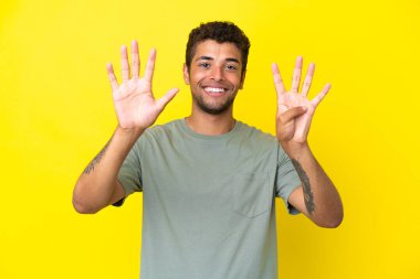 Sarı arka planda izole edilmiş yakışıklı Brezilyalı dokuz parmağıyla sayıyor.