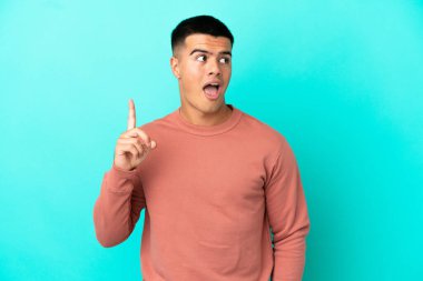 Soyutlanmış mavi arka planda genç yakışıklı bir adam bir fikir düşünüyor.