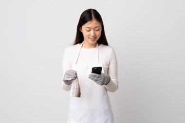 Çinli balıkçı önlük takıyor ve beyaz arka planda çiğ balık tutuyor. Cep telefonuyla bir mesaj gönderiyor.