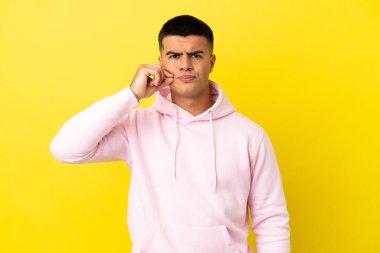 Soyutlanmış sarı arka planda genç yakışıklı bir adam sessizlik işareti gösteriyor.