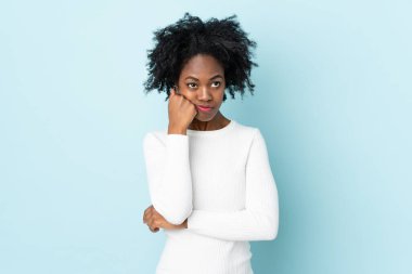 Genç Afrikalı Amerikalı kadın mavi arka planda izole edilmiş, yorgun ve sıkılmış bir ifadeyle.