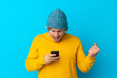 Yakışıklı sarışın adam mavi arka planda izole edildi. Şaşırdı ve bir mesaj gönderiyor.