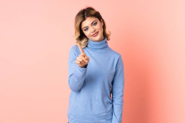 Pembe arka planda izole edilmiş genç Rus kadın parmağını kaldırıyor ve gösteriyor.