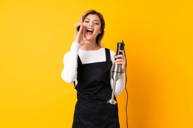 El blenderi kullanan kız sarı arka planda izole edilmiş bağırıyor ve bir şey duyuruyor.
