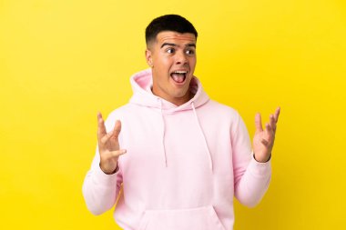 Sürpriz yüz ifadesi ile izole sarı arka plan üzerinde genç yakışıklı adam