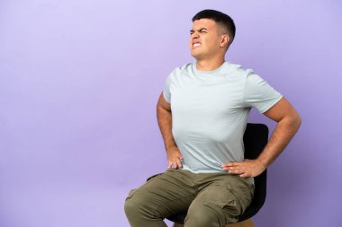 Arka planda izole edilmiş bir sandalyede oturan genç adam gayret gösterdiği için sırt ağrısından muzdarip.