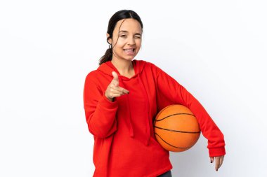 İzole edilmiş beyaz arka planda basketbol oynayan genç bir kadın öne doğru bakıyor ve gülümsüyor.