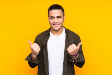 Asyalı yakışıklı adam sarı arka planda izole edilmiş düşünüyor.