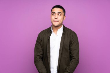 Asyalı yakışıklı adam mavi arka planda izole edilmiş, yukarı bakarken şüpheleri var.