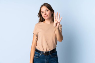 Genç Litvanyalı kadın mavi arka planda izole edilmiş mutlu ve parmaklarıyla dörde kadar sayıyor.