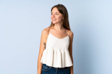 Genç Litvanyalı bir kadın mavi arka planda izole edilmiş, yana bakıyor ve gülümsüyor.