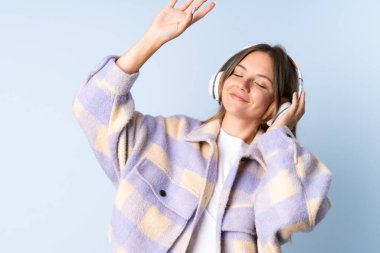 Genç Litvanyalı kadın mavi arka planda izole edilmiş müzik ve dans dinliyor.