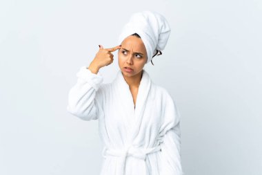 Bornozlu genç bir kadın, izole edilmiş beyaz bir arka planı var. Delilik jesti yapıyor. Parmağını kafaya koyuyor.