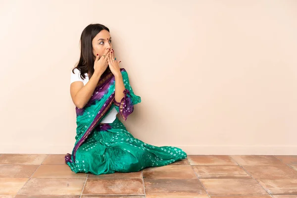 年轻的印度妇女坐在地板上捂住嘴 朝旁边看去 — 图库照片