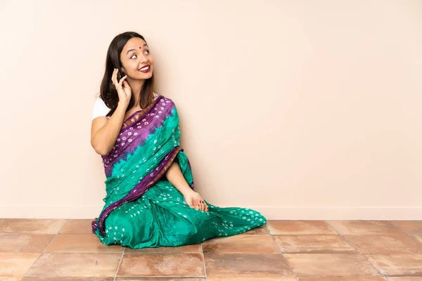 年轻的印度女人坐在地板上和别人用手机交谈 — 图库照片