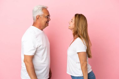 Mutlu bir ifadeyle pembe arka planda izole edilmiş orta yaşlı bir çift.