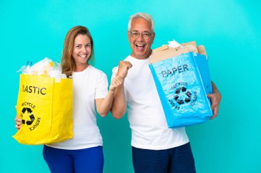 Orta yaşlı bir çift ellerinde kağıt ve plastikle dolu bir geri dönüşüm çantası tutarak zaferi kutluyorlar.