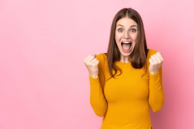 Pembe arka planda izole edilmiş genç beyaz kadın galibiyeti kutluyor.