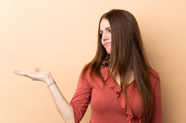 Beyazlı genç bir kadın bej arka planda izole edilmiş. Kopyalama alanını şüphe ile tutuyor.