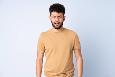 Faslı genç bir adam mavi arka planda izole edilmiş ve yüzünde sürpriz bir ifade var.