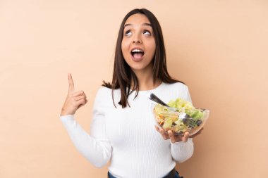 Genç esmer kız izole edilmiş arka planda salata tutuyor.