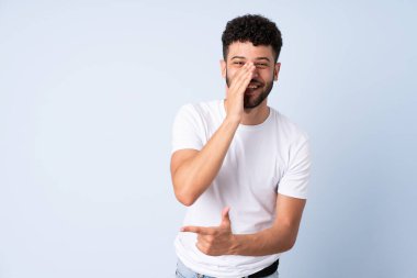 Mavi arka planda izole edilmiş genç Faslı bir adam bir ürün sunmak ve bir şeyler fısıldamak için kenarı işaret ediyor.