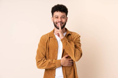 Bej arka planda izole edilmiş genç Faslı bir adam sessiz bir jest işareti gösteriyor. Parmağını ağzına sokuyor.