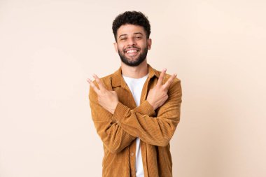 Bej arka planda izole edilmiş genç Faslı adam gülümsüyor ve zafer işareti gösteriyor.
