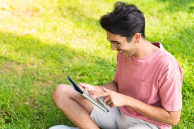 Parkta elinde mutlu bir ifadeyle tablet tutan beyaz bir genç.