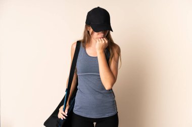 Spor çantası tutan Litvanyalı genç bir kadın. Bej arka planda izole edilmiş. Şüpheleri var.