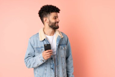 Pembe arka planda izole edilmiş cep telefonu kullanan Faslı genç adam.
