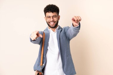 Faslı genç bir iş adamı bej arka planda izole edilmiş. Gülümserken parmağıyla seni işaret ediyor.